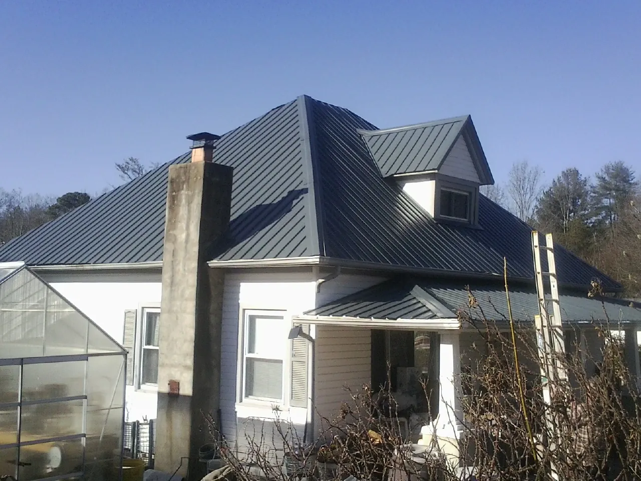 Dark blue standing seam metal roof on a white farmhouse with dormer — Slate & Tile Roof Repair by Roofing Brothers in Beach Lake