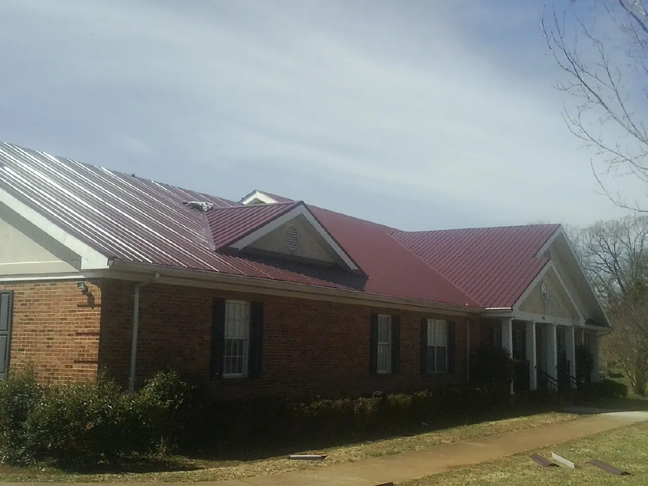 Red metal roof with gabled entries on a long brick building, from a Hail Damage Roof Repair job in Beach Lake