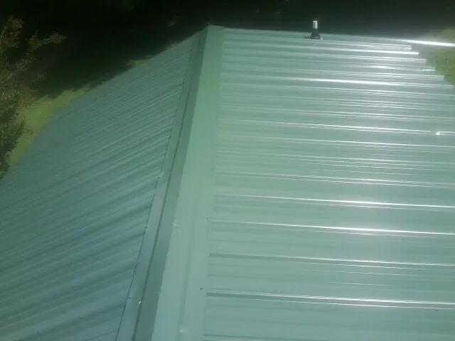 New green metal panels meeting at the ridge of a roof — Flat Roof Repair work by our crew in Beach Lake