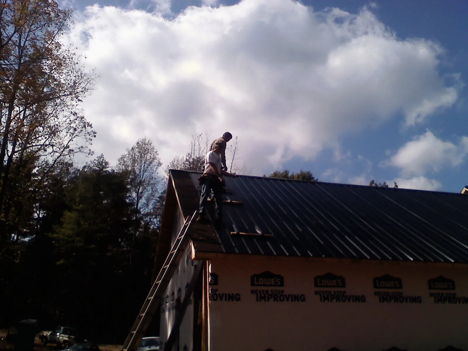 Roofer fastening dark metal panels high against a cloudy sky, from a Roof Inspection job in Beach Lake