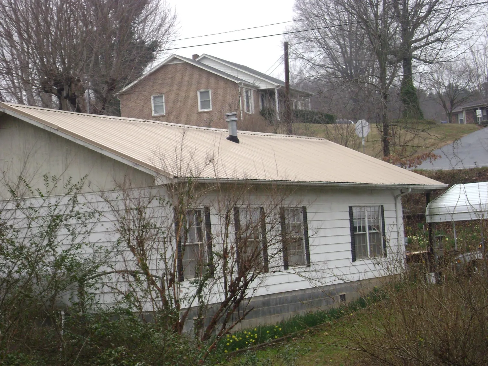 Tan metal roof on a white sided house set into a hillside — Commercial Roofing by Roofing Brothers in Beach Lake
